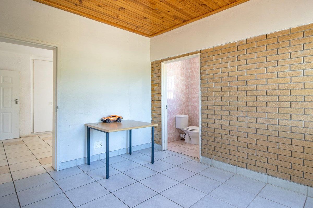 A bedroom featuring an exposed brick feature wall, timber ceiling, and tiled flooring, with direct access to an en-suite bathroom.