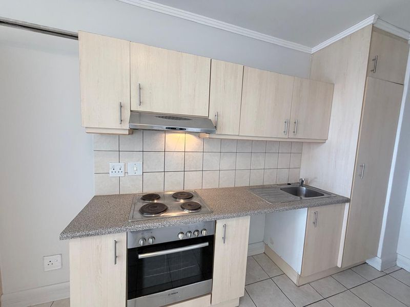 A functional kitchen featuring light wood-finish cabinetry, a tiled backsplash, integrated electric hob and oven, and a stainless steel sink.