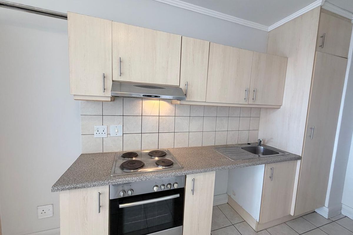 A functional kitchen featuring light wood-finish cabinetry, a tiled backsplash, integrated electric hob and oven, and a stainless steel sink.