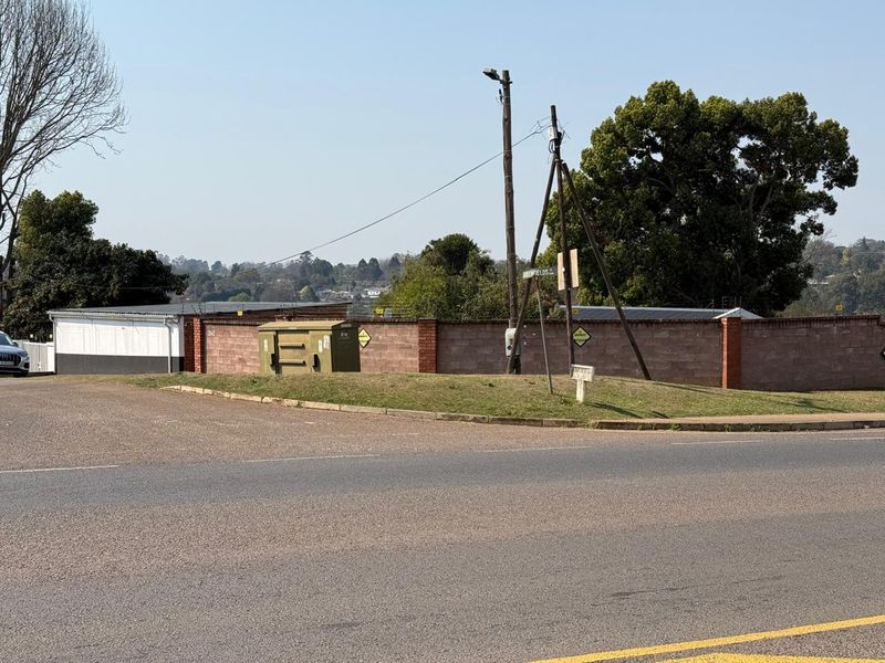 Street view showing the property boundary wall, utility infrastructure, and surrounding road access.
