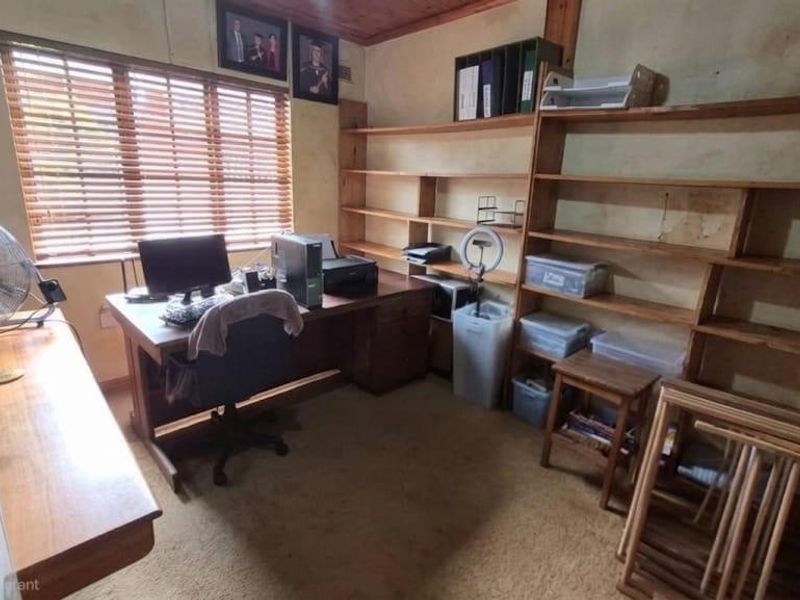 A home office featuring built-in wooden shelving, timber ceiling details, and venetian blinds, offering a functional workspace with potential for cosmetic updates.