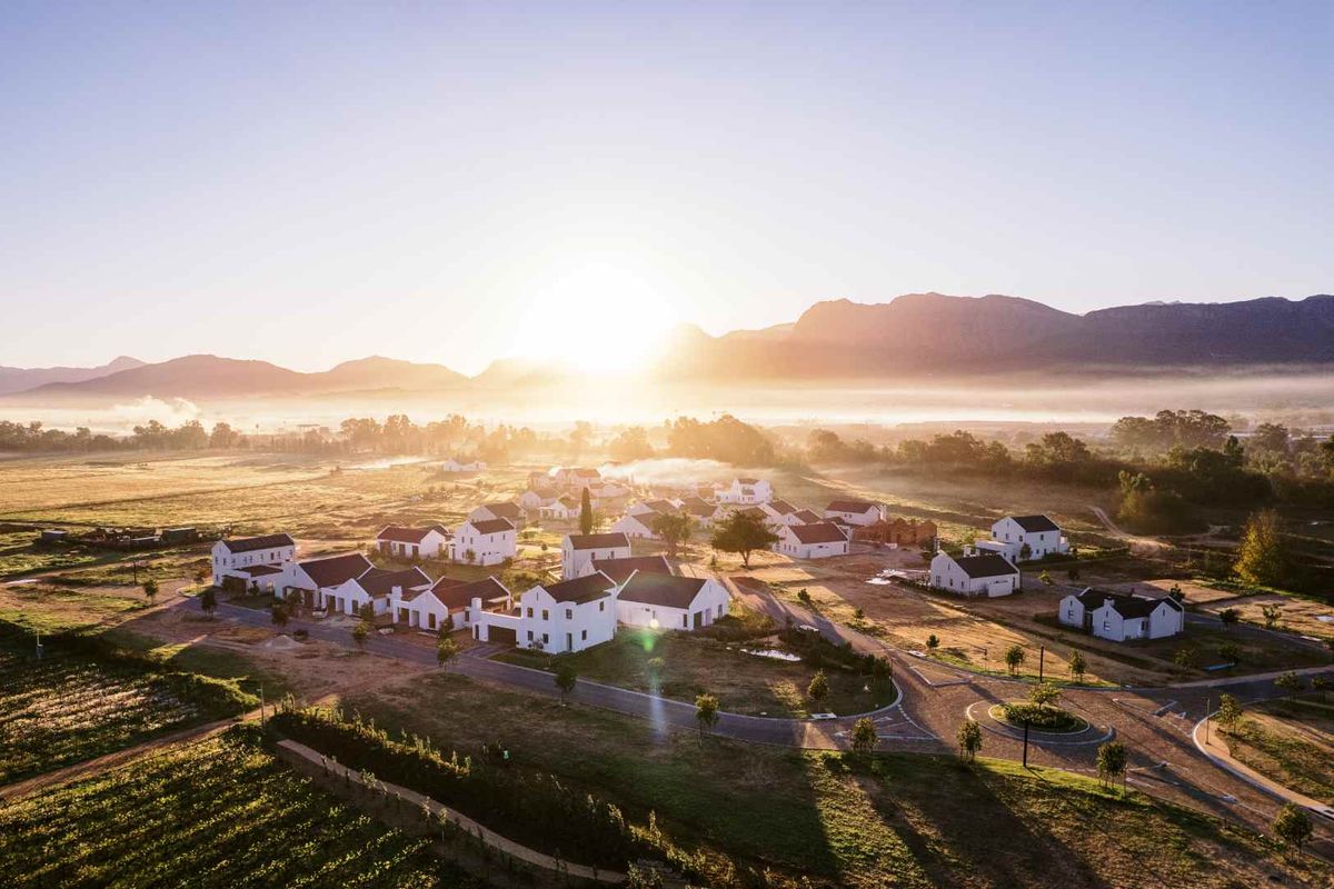 An aerial view of a residential estate featuring white houses with dark roofs, set against a scenic mountain landscape at sunrise.