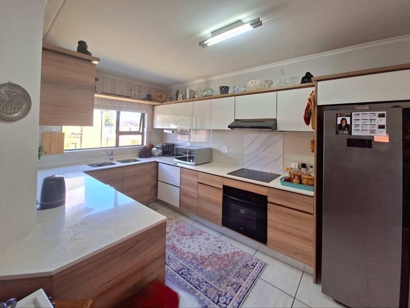 Modern kitchen featuring wood-grain and white cabinetry, stone countertops, integrated electric hob, oven, extractor fan, and tiled flooring.