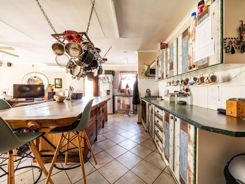 Open-plan kitchen and living area featuring tiled flooring, custom cabinetry, a built-in oven, and a central island with a hanging pot rack.