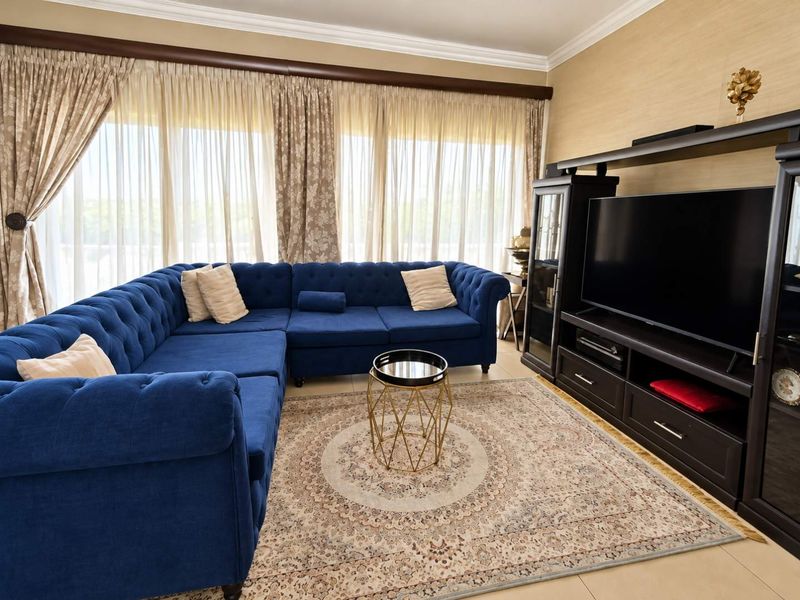 A well-maintained living room featuring tiled flooring, crown molding, and large windows with floor-to-ceiling curtains, providing a bright and comfortable living space.