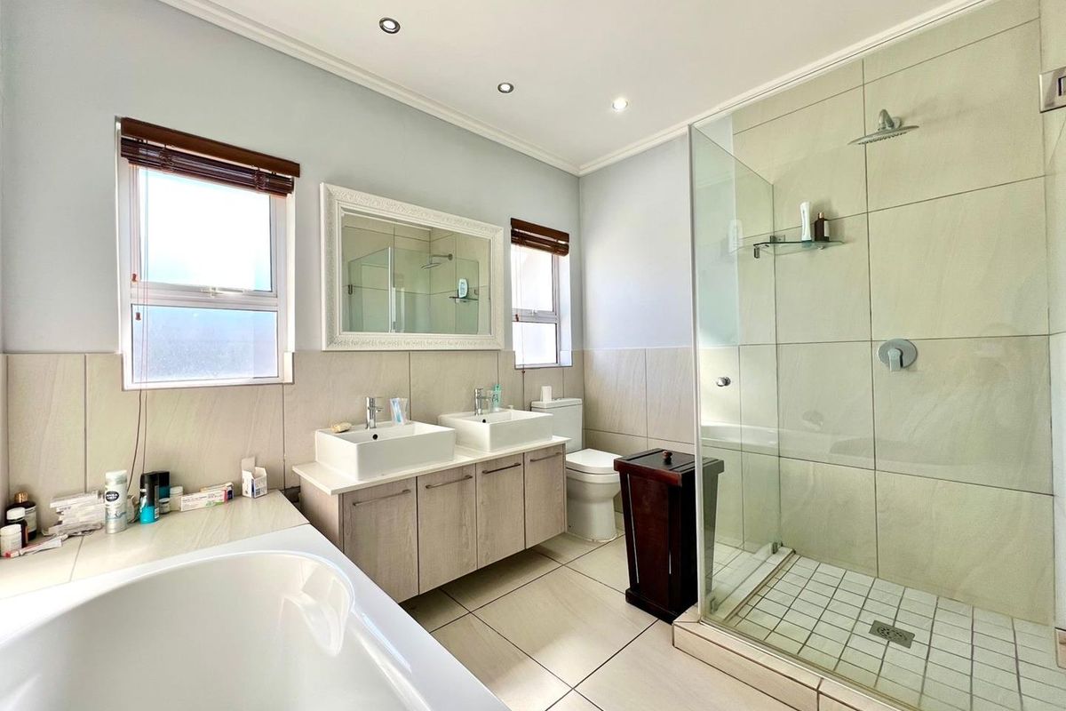 Modern bathroom featuring a double vanity, glass-enclosed walk-in shower, and a separate bathtub with neutral tiled finishes and recessed lighting.