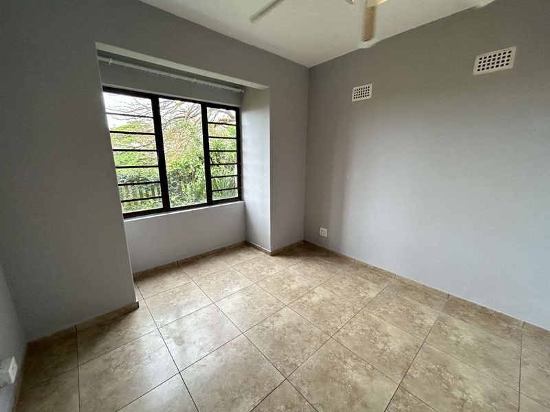 A bright, empty bedroom featuring neutral grey walls, tiled flooring, and a ceiling fan, offering a clean canvas for personalization.