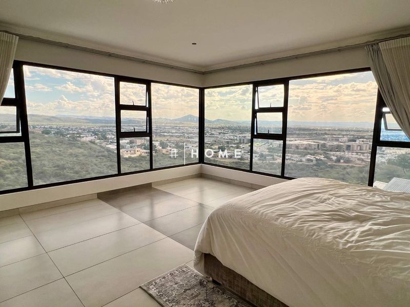 Spacious bedroom featuring expansive corner windows that offer panoramic views and abundant natural light, complemented by neutral tiled flooring.