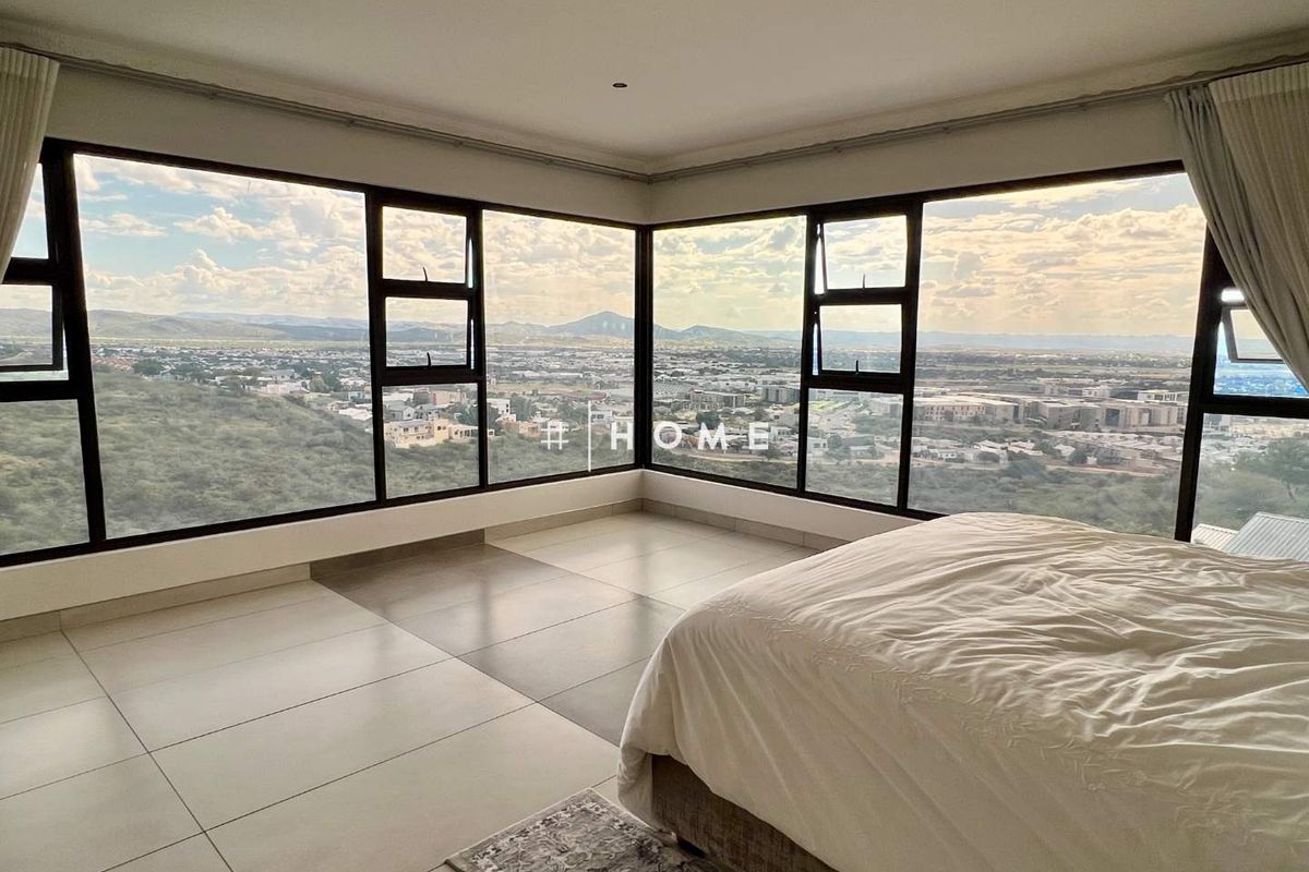 Spacious bedroom featuring expansive corner windows that offer panoramic views and abundant natural light, complemented by neutral tiled flooring.