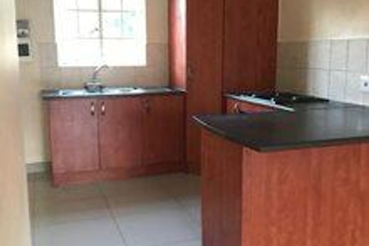 A functional kitchen featuring built-in wooden cabinetry, laminate countertops, a stainless steel sink, and tiled flooring in a clean, empty space.
