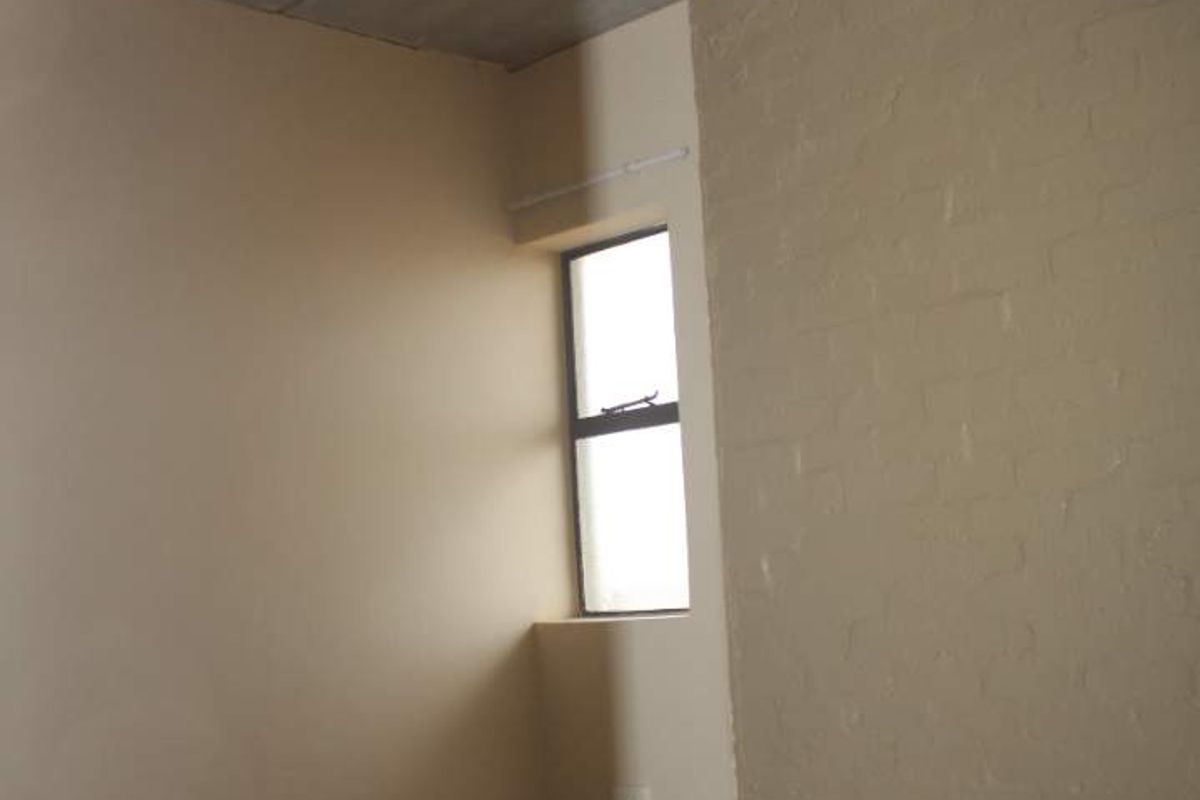 An empty bedroom featuring tiled flooring, a textured brick accent wall, and an exposed concrete ceiling with a central light fixture.