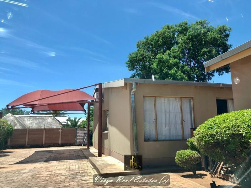 Exterior view of the property featuring a paved driveway, shade sail structure, and perimeter boundary wall with electric fencing.