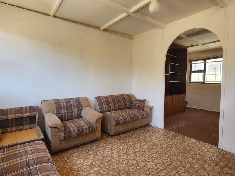 A dated living room featuring an arched entryway, built-in shelving, and exposed beam ceilings, requiring significant cosmetic updates and renovation.