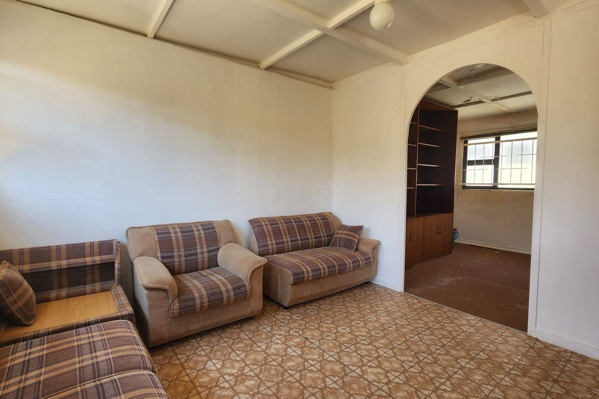 A dated living room featuring an arched entryway, built-in shelving, and exposed beam ceilings, requiring significant cosmetic updates and renovation.