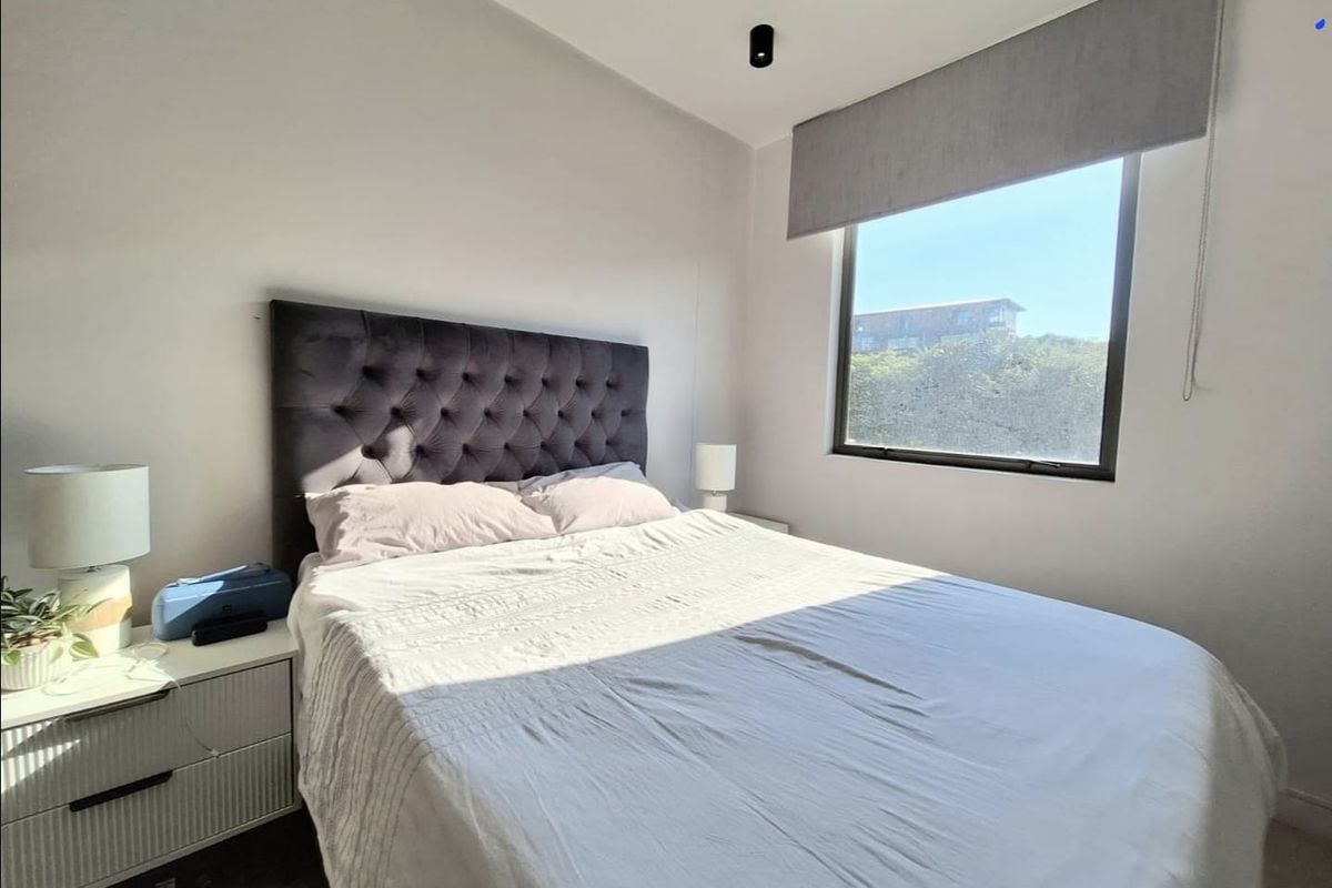 A well-lit bedroom featuring a large window with a roller blind and modern ceiling lighting, creating a bright and comfortable living space.
