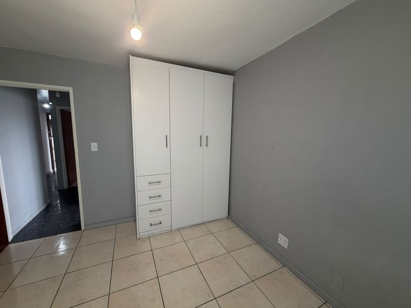 A clean, empty bedroom featuring neutral grey walls, tiled flooring, and a white built-in wardrobe with integrated drawer storage.