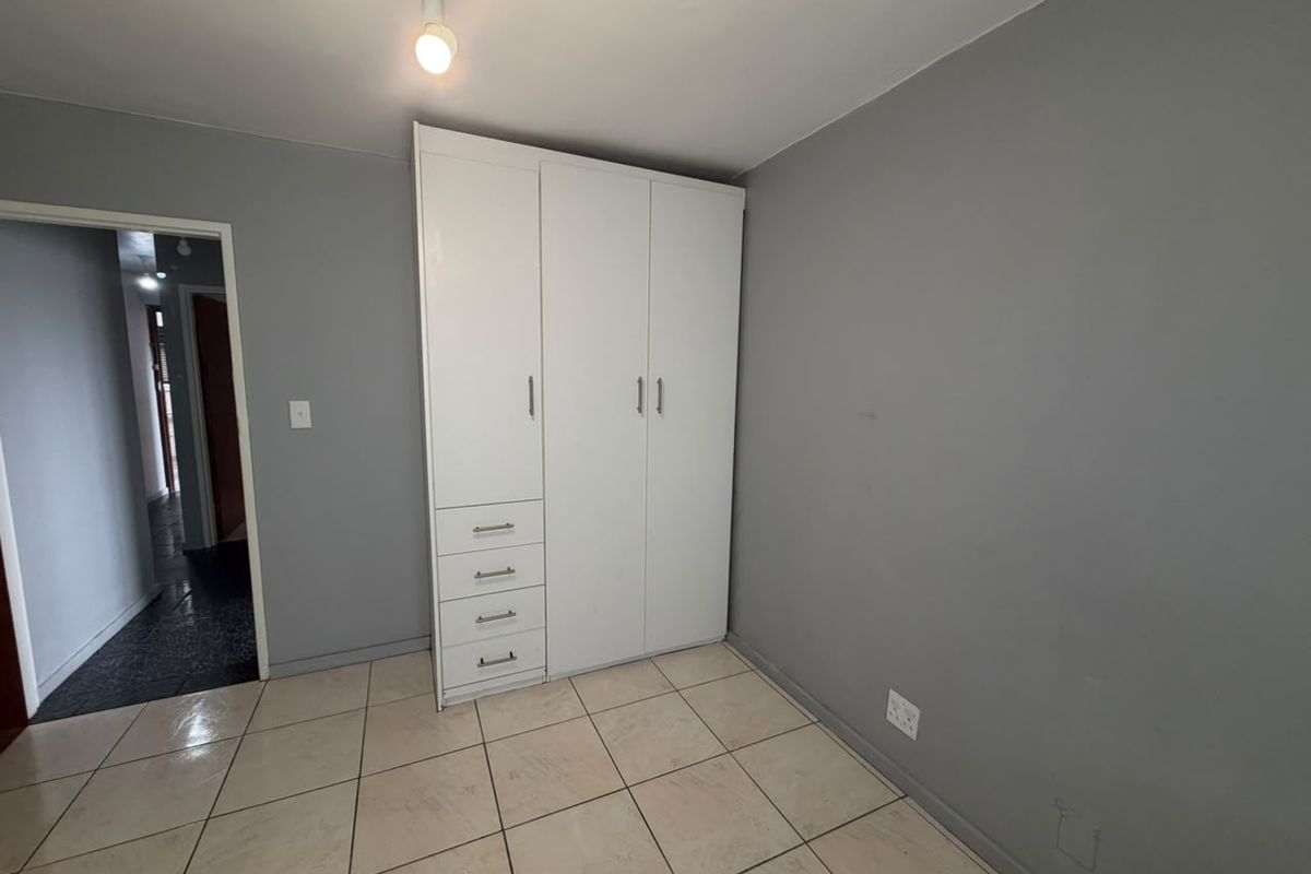 A clean, empty bedroom featuring neutral grey walls, tiled flooring, and a white built-in wardrobe with integrated drawer storage.