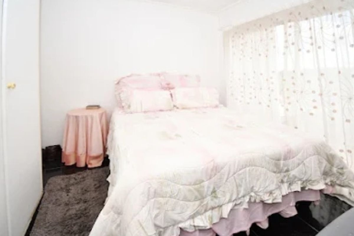 A compact bedroom featuring a built-in wardrobe and large window with sheer curtains, offering a functional and neutral living space.