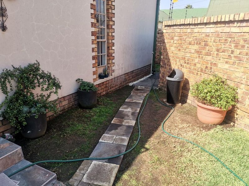 A side garden area featuring a paved walkway, brick boundary wall, and plastered exterior wall with brick detailing.
