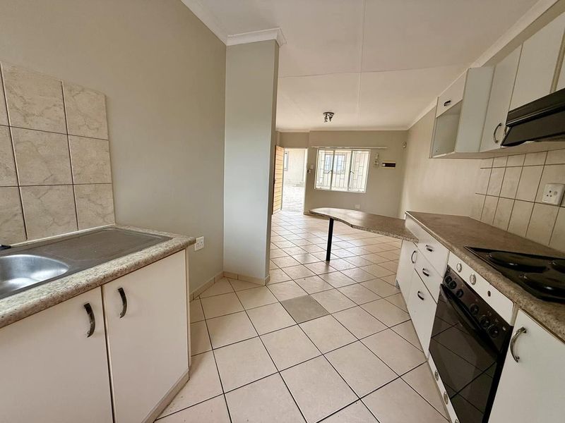 Open-plan kitchen and living area featuring tiled flooring, built-in cabinetry, integrated oven and hob, and a breakfast bar counter.