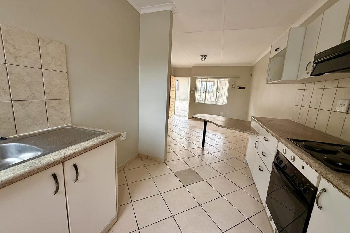 Open-plan kitchen and living area featuring tiled flooring, built-in cabinetry, integrated oven and hob, and a breakfast bar counter.
