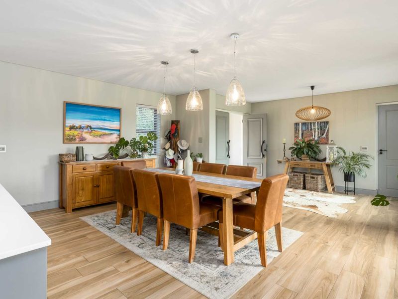 A bright and well-maintained dining area featuring modern laminate flooring, elegant pendant lighting, and neutral wall finishes.