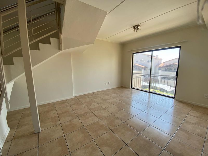 An empty living room featuring tiled flooring, a staircase, and a sliding glass door leading to a balcony.