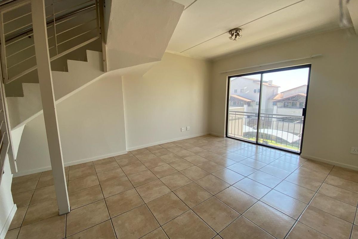 An empty living room featuring tiled flooring, a staircase, and a sliding glass door leading to a balcony.