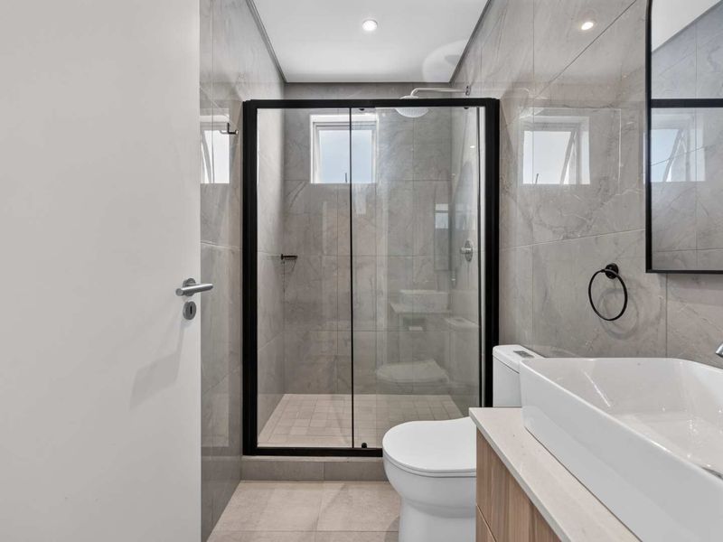 Modern bathroom featuring a walk-in shower with black-framed glass, a sleek vanity with a vessel sink, and contemporary grey wall tiling.