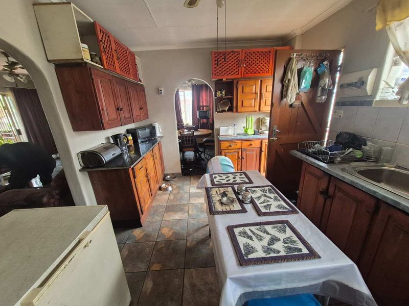 A dated kitchen featuring wooden cabinetry, stone countertops, and tiled flooring, with arched doorways leading to adjacent living spaces.