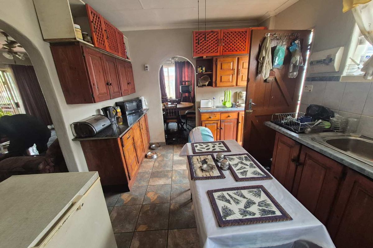 A dated kitchen featuring wooden cabinetry, stone countertops, and tiled flooring, with arched doorways leading to adjacent living spaces.