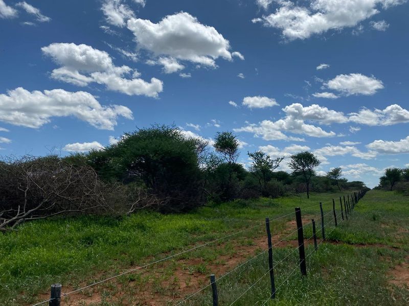 An expansive outdoor view of the small holding featuring natural vegetation, open green space, and perimeter wire fencing with wooden posts.