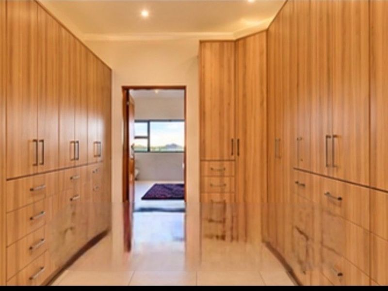 Spacious walk-in dressing area featuring extensive floor-to-ceiling wood-finish built-in cabinetry and tiled flooring, leading through to an adjoining room.