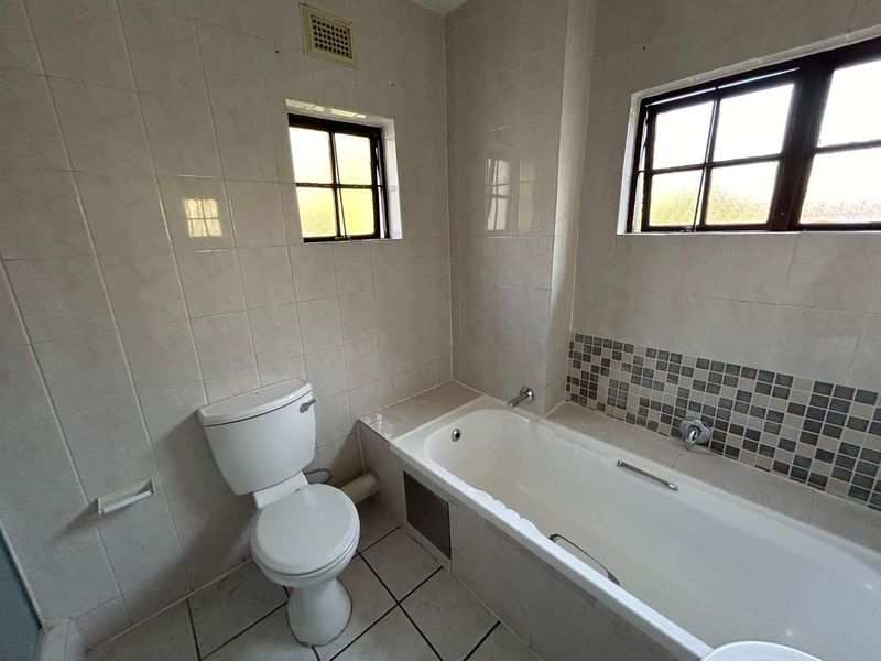 A functional bathroom featuring a bathtub, toilet, and neutral wall tiling with mosaic accent detailing.