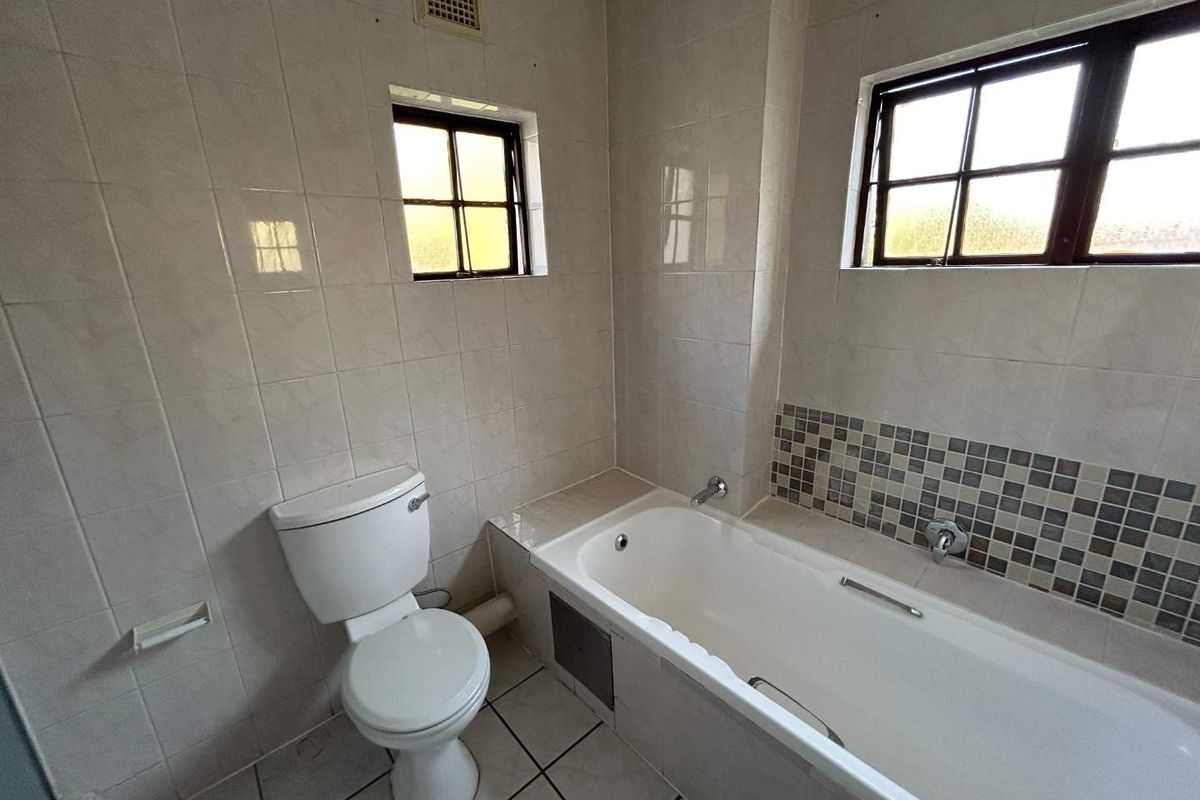 A functional bathroom featuring a bathtub, toilet, and neutral wall tiling with mosaic accent detailing.