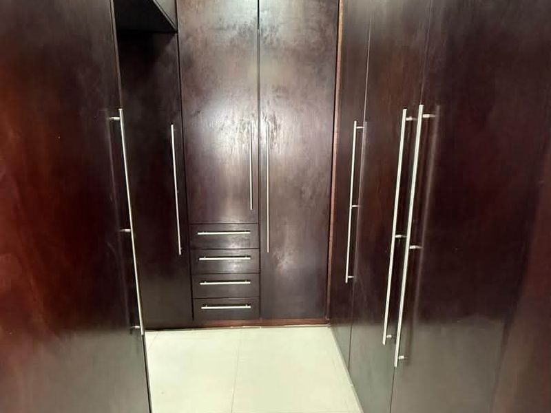 A walk-in closet area featuring extensive dark wood built-in cabinetry and light-colored floor tiles.
