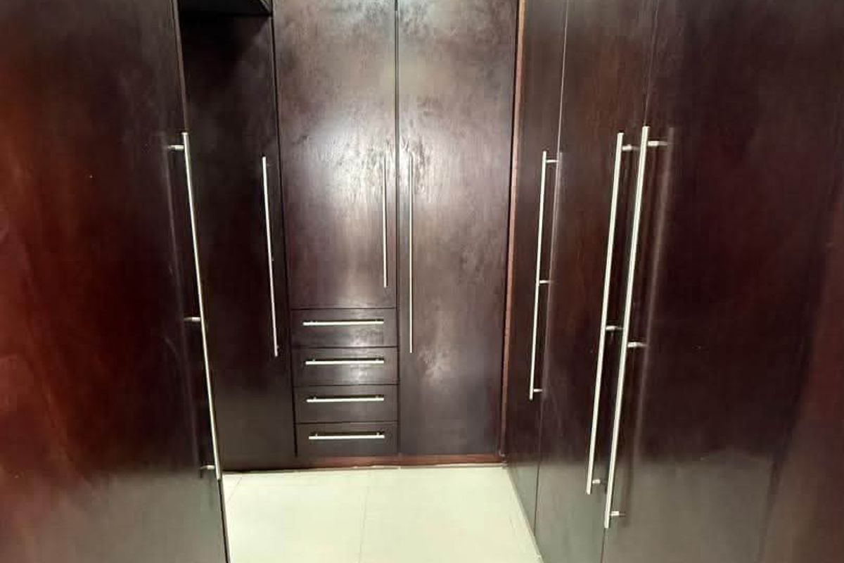 A walk-in closet area featuring extensive dark wood built-in cabinetry and light-colored floor tiles.