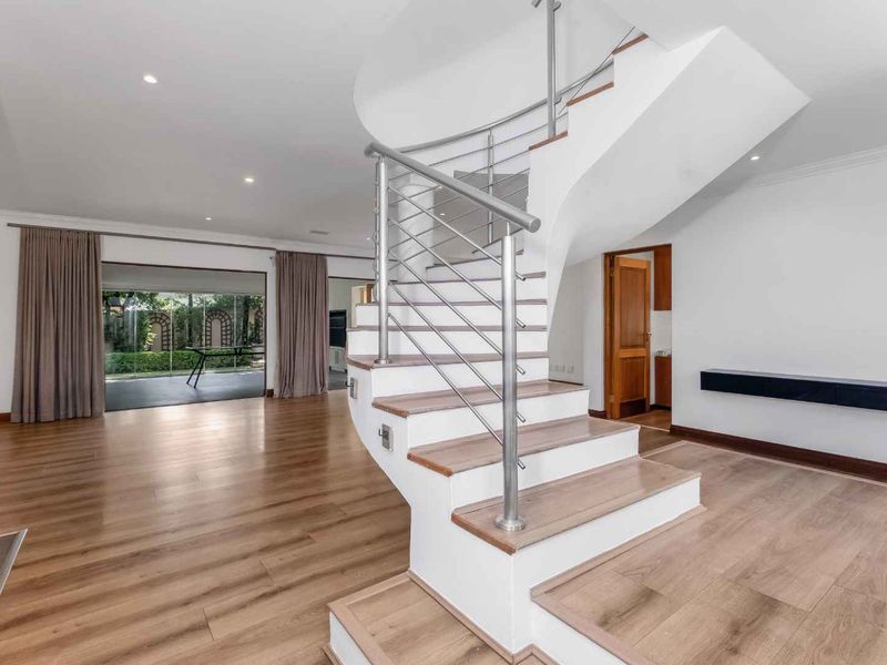 Spacious living area featuring a modern spiral staircase with stainless steel balustrade, laminate flooring, and large sliding doors leading to the patio.