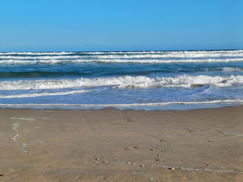 A scenic view of the ocean waves crashing onto the sandy beach, highlighting the coastal location of the property.