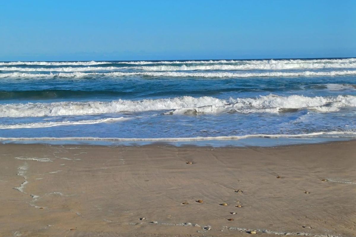 A scenic view of the ocean waves crashing onto the sandy beach, highlighting the coastal location of the property.