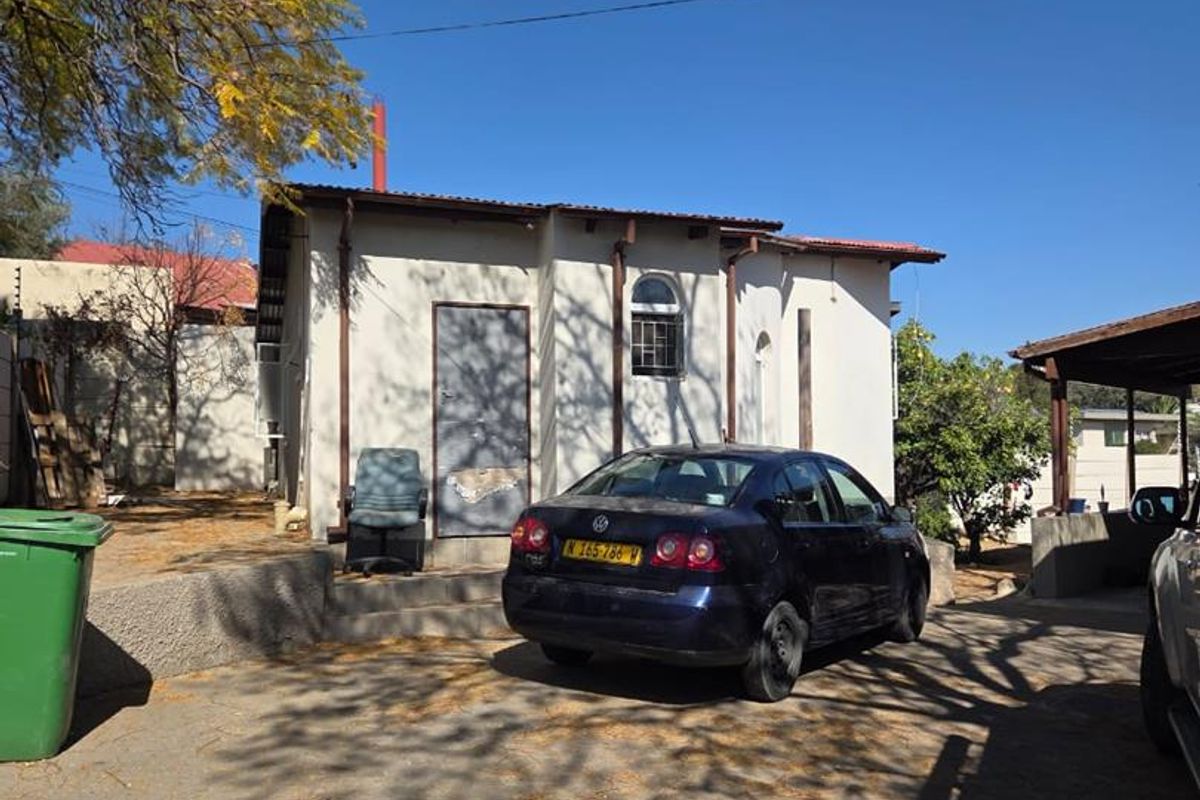 Rear exterior view of the property featuring a paved driveway, carport, and basic building facade with a metal door and arched window.