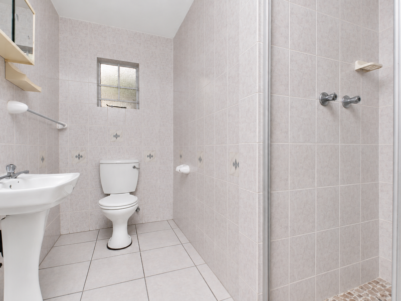 A functional bathroom featuring a pedestal washbasin, toilet, and a shower enclosure with tiled walls and flooring throughout.