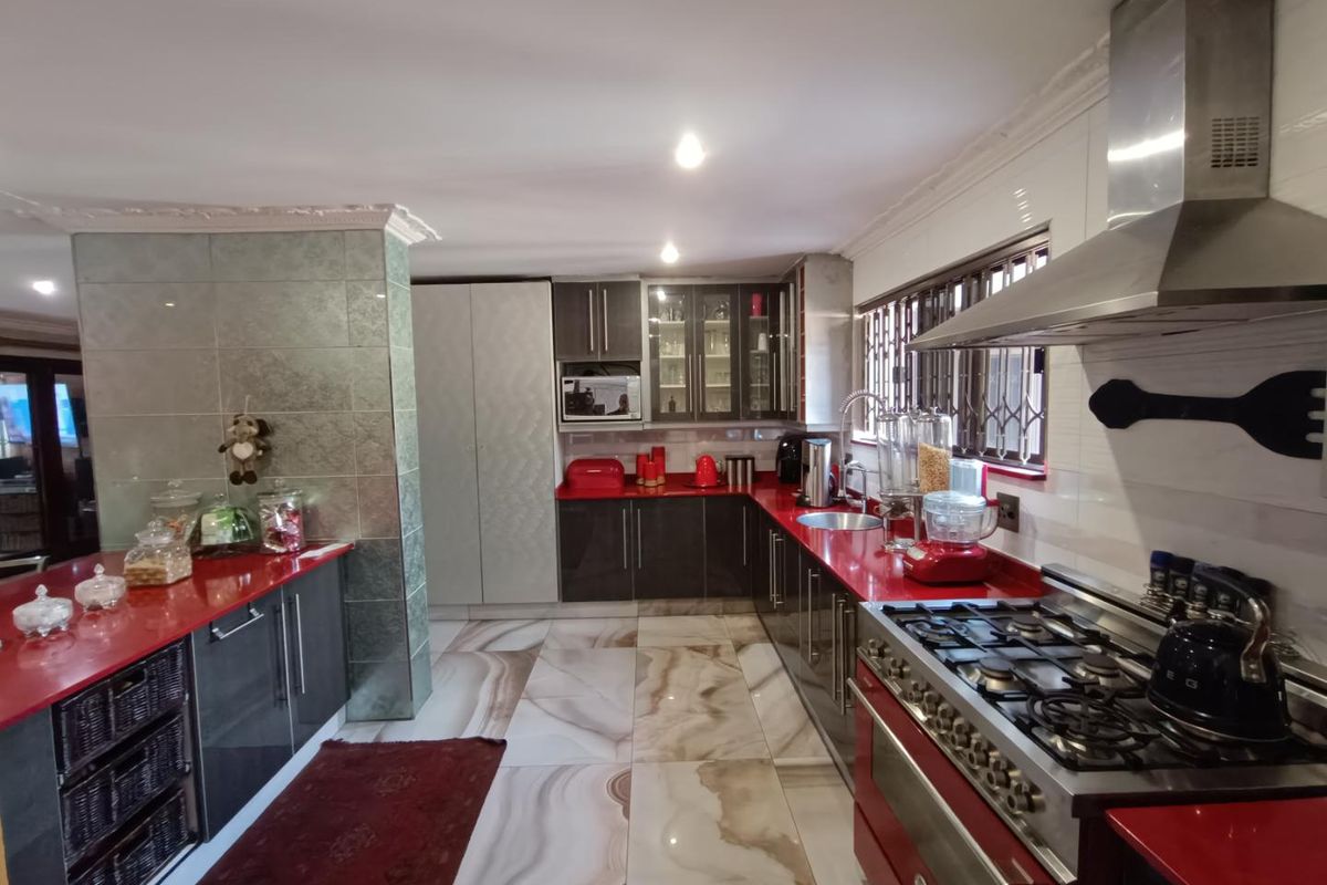 Modern kitchen featuring high-gloss cabinetry, vibrant red countertops, large-format marble-look floor tiles, and a professional-grade stainless steel gas range with extractor hood.