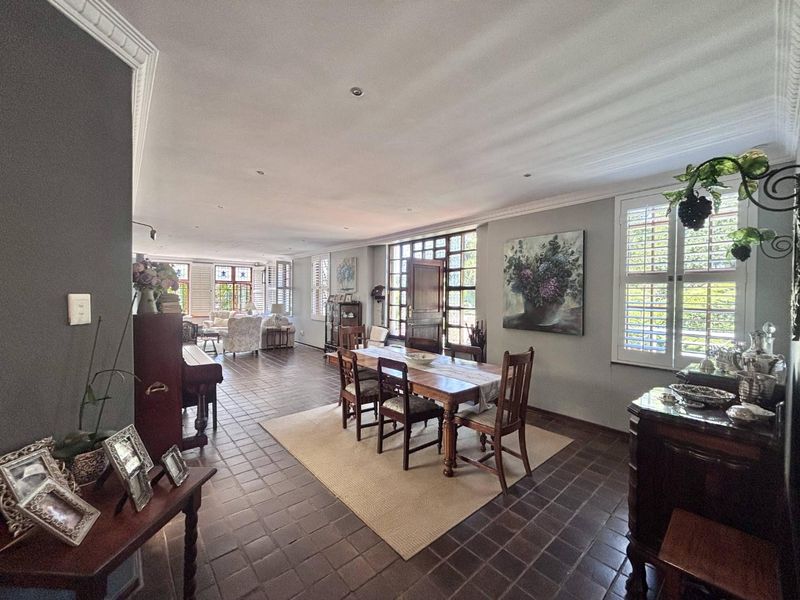Spacious open-plan living and dining area featuring classic terracotta tile flooring, elegant crown molding, and large timber-framed windows with plantation shutters.