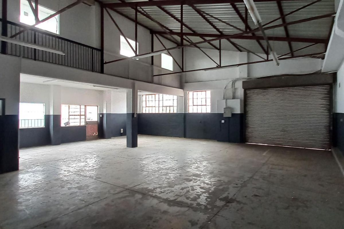 Spacious industrial utility area featuring high ceilings with exposed steel trusses, a large roller shutter door, concrete flooring, and a mezzanine level.