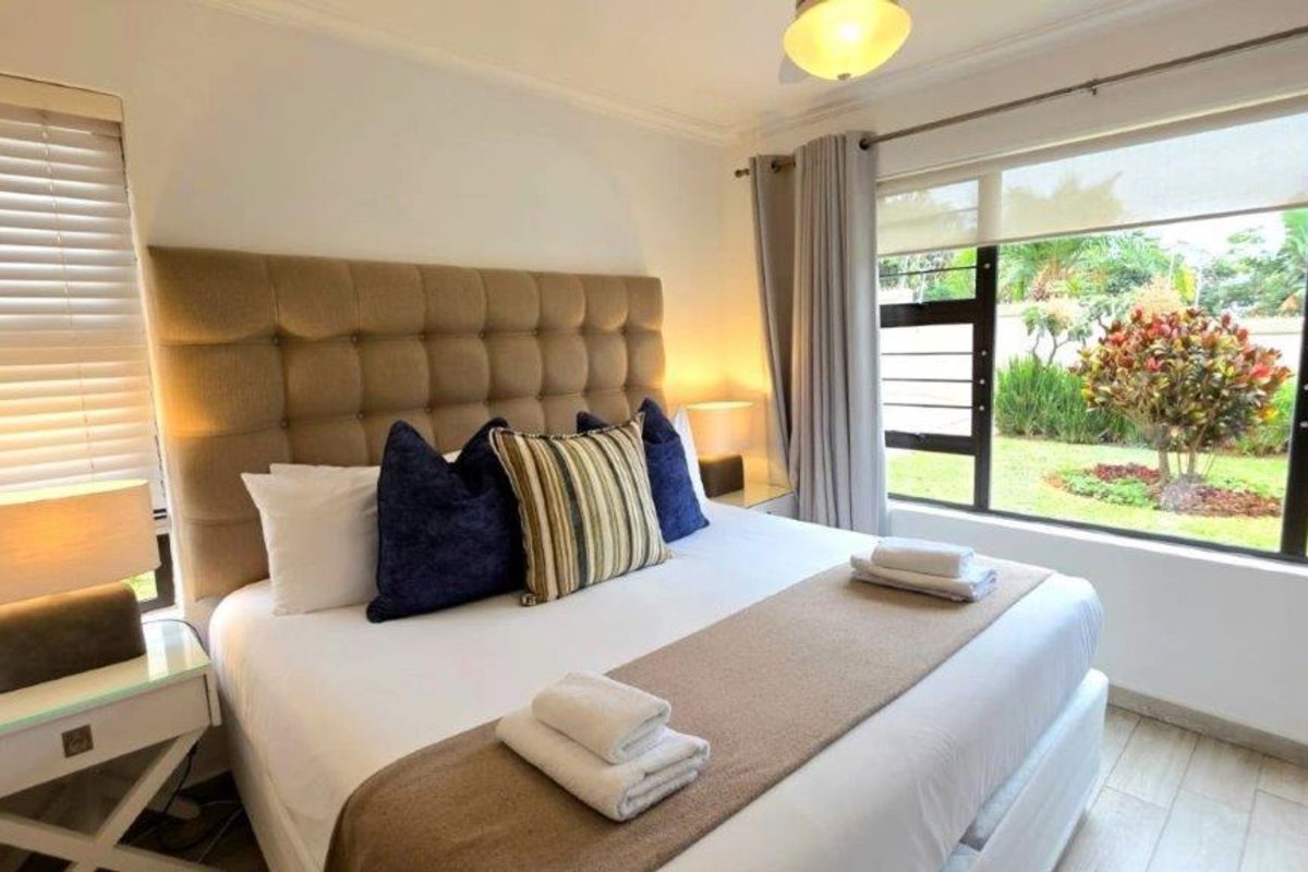 A bright and well-maintained bedroom featuring large windows with garden views, tiled flooring, and neutral finishes.