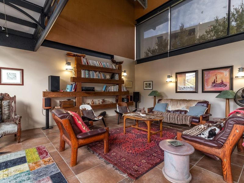 Spacious living room featuring high ceilings, exposed steel structural beams, large clerestory windows, tiled flooring, and custom built-in timber shelving.