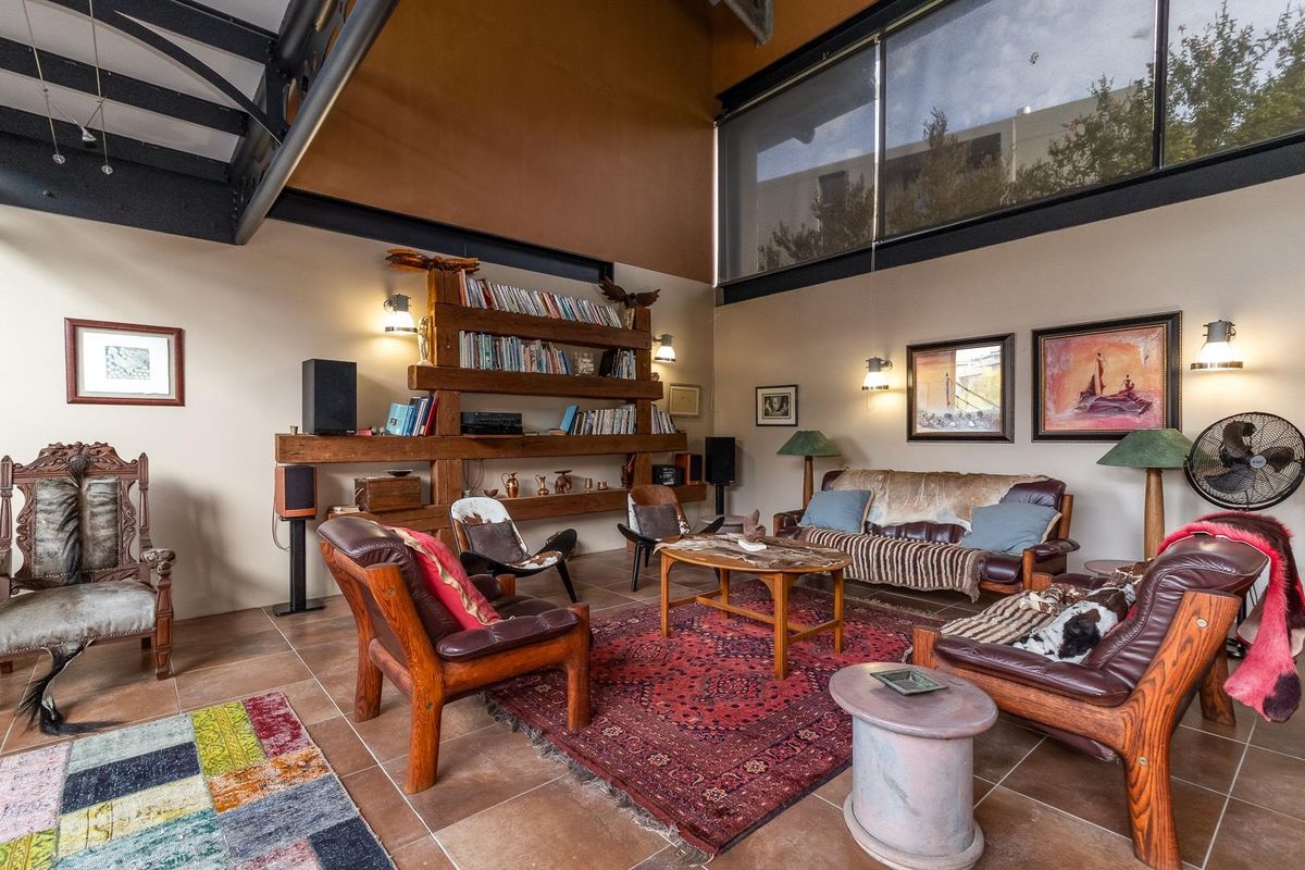 Spacious living room featuring high ceilings, exposed steel structural beams, large clerestory windows, tiled flooring, and custom built-in timber shelving.