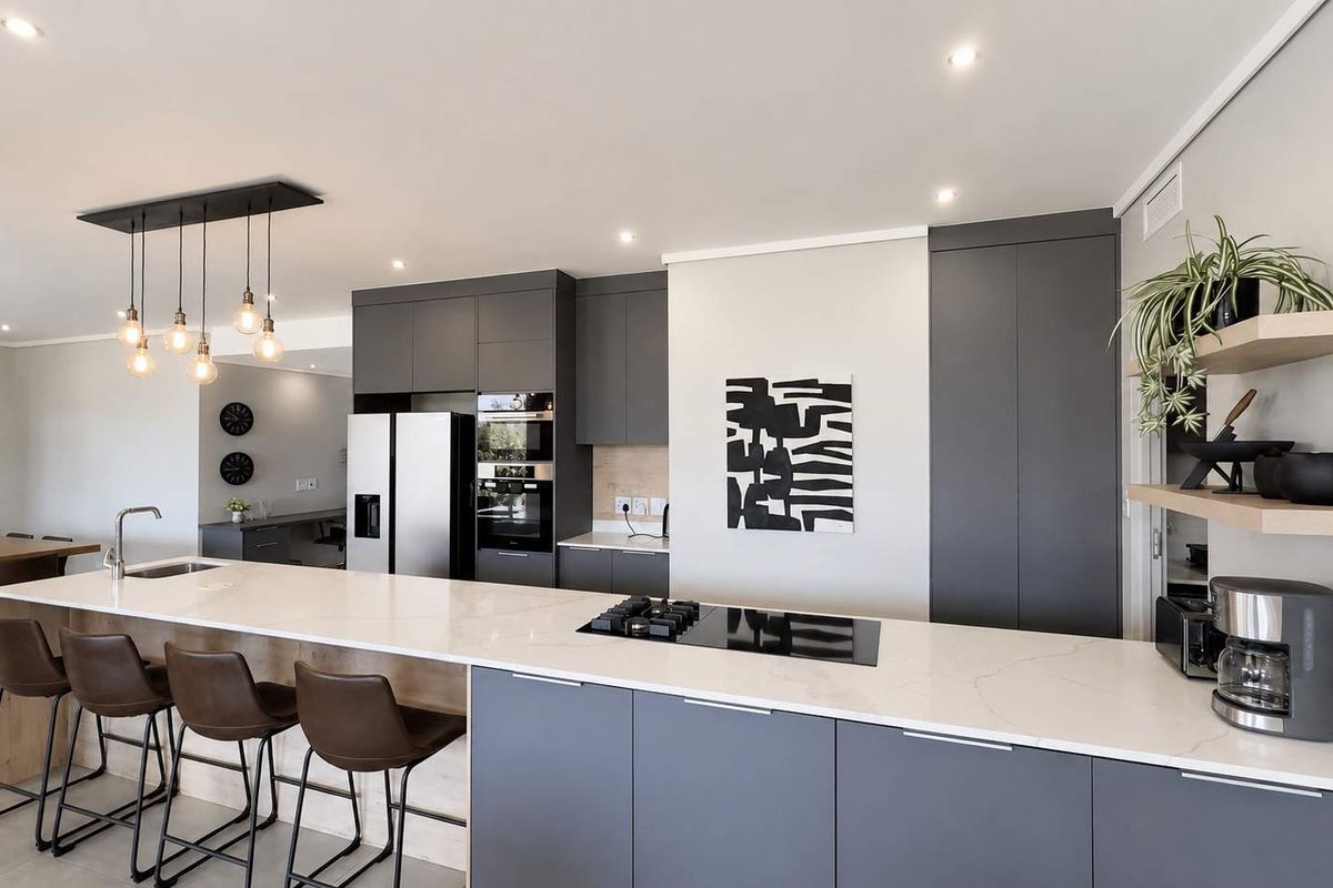 Modern open-plan kitchen featuring dark grey cabinetry, a large quartz island with integrated gas hob, and high-end built-in appliances.