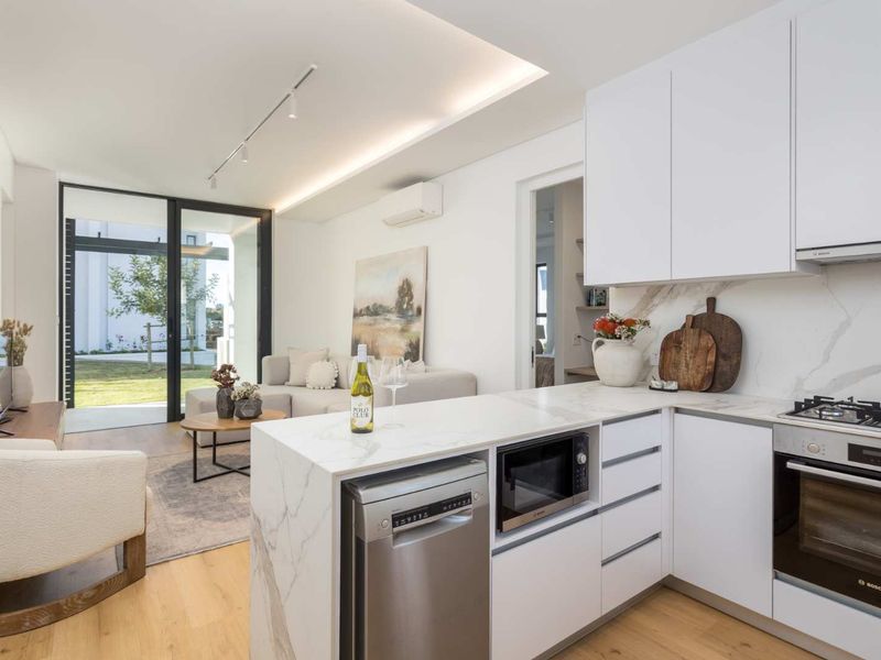 Modern open-plan living area featuring a sleek kitchen with stone countertops, integrated appliances, recessed lighting, and seamless access to the outdoor patio.